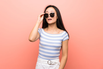 Teenager asian girl over isolated pink background with glasses and surprised