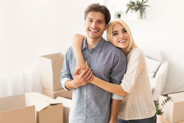 Young Couple Hugging Posing Among Moving Boxes In New Home