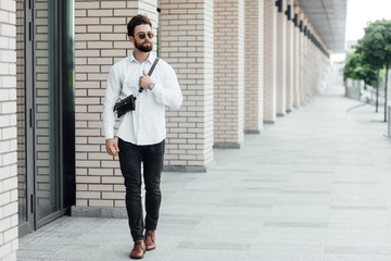 A bearded, serious, stylish man walking  on the streets of the city near modern office centre. Copy space.