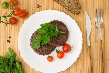 Ground beef meat Burger steak cutlets in a white plate on a wooden board background. Cutlet for burger with vegetables