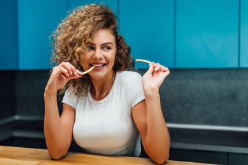 Fototapeta premium Time for fast food, blonde young girleat french fries at home.