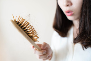 Young asian woman worried about hair loss after brushing her hair with comb. Hair problems and health care concept. Close up.