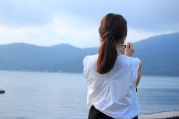 A woman is taking a photo in front of beautiful lake.