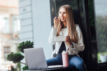 Pretty blonde girl have a breakfast with lunch box, while sitting near building.