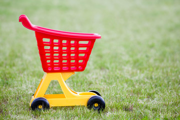 Bright plastic colorful shopping cart toy outdoors on sunny summer day.