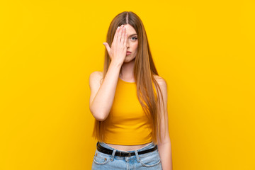 Fototapeta premium Young woman over isolated yellow background covering a eye by hand