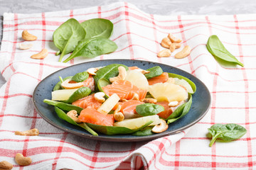 Fresh salmon with pineapple, spinach and cashew in blue ceramic plate on a gray concrete background.