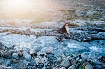 A young woman with backpack crossing the cold river in Patagonia, Chile. Sun set and taking shoes after a river crossing. Winter backpacking in South America.