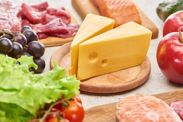 Cheese on wooden cutting board near assorted meat, fish fruits and vegetables