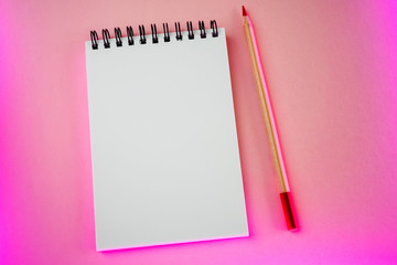 An open white notebook on a spiral and a red pencil lies on a pink paper background with a neon stylish trend highlight. Place for text. Concept of ideas, notes. Minimalism, flat lay, top view. - Powered by Adobe