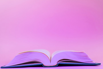 Close-up book on a pastel pink background in a trendy neon color light. The concept of reading, book novelties, book business, literature. Minimalism, place for text.