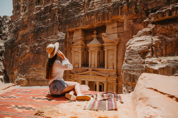 Young woman tourist sitting on a cliff after reaching the top, Al Khazneh in the ancient city of Petra, Jordan, UNESCO World Heritage Site - obrazy, fototapety, plakaty