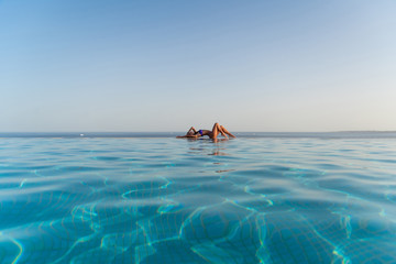 Attractive young woman in bikini leaning on the edge of infinity swimming pool.