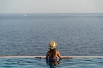 Foto op Canvas Beautiful young woman with a hat is relaxing in an infinity pool with a breathtaking view © F8  \ Suport Ukraine