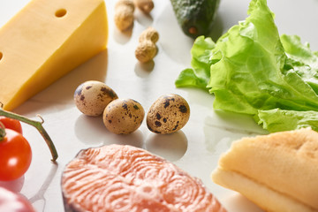 Close up view of raw salmon steak near quail eggs, cheese, lettuce, tomatoes and peanuts on white...