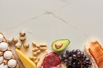 Top view of raw meat and fish with eggs, avocado, cheese, grapes and peanuts