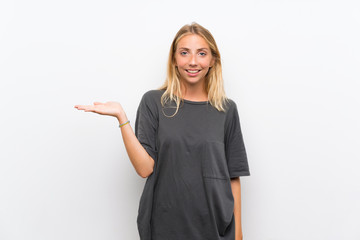 Blonde young woman over isolated white background holding copyspace imaginary on the palm to insert...