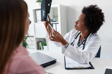A female doctor sits at her desk and talks to a female patient while looking at her mamogram. Brest...