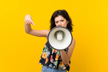 Young woman over isolated yellow background shouting through a megaphone