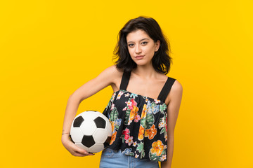 Young woman over isolated yellow background holding a soccer ball