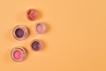 Cosmetics. Makeup. Jars with  crumbly bright shadows, glitter. Pink,peach, golden colors on beige background. Closeup. Space for text or design.