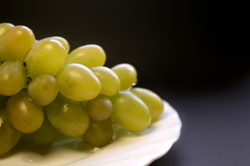 Bunch of green grape isolated on a plate on a black background
