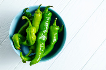 Hot, spicy green peppers in a blue bowl on a white wooden background with copy space. Top view...