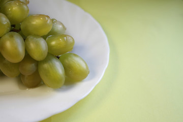 bunch of green grapes in a white plate on a yellow background