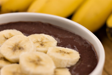 bowl of acai smoothie with banana slices on top and bunch of bananas in the background