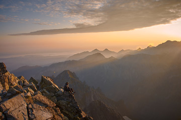 Plakat Man hiker sitting on the peak of mountain looking on sunrise