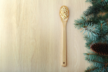 Cedar pine nuts in wooden spoon with cones, cedar brunch on wooden background. Top view witn copy space.