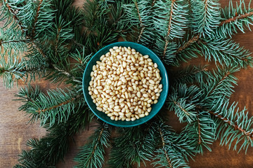 Cedar pine nuts in green plate with cedar brunch on wooden background. Top view.