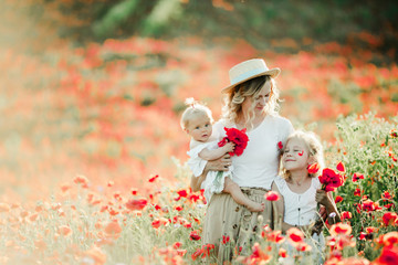 mother holds her hat, baby looks at her sister her baby and looks at her elder daughter on the poppy field