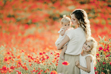mother looks at her baby, elder daughter nestles to mom on the poppy field