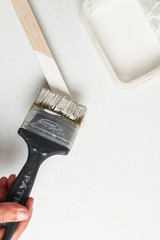 Mano con brocha negra pintando con pintura blanca palo de madera sobre un fondo blanco y tarro de...