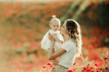 a woman smiles to a baby on the poppy field