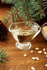 Pine nut oil and bowl of pine nuts on wooden background with cones, cedar brunches.