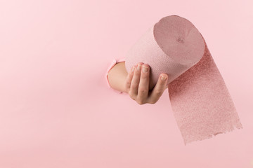 Woman hand holds toilet paper from a hole in a pink background. Concept, copy space.