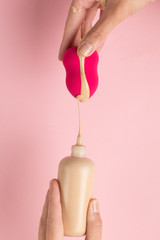 Girl hand holds beauty blender in foundation, concealer on pink background. Makeup artist concept, copy space.