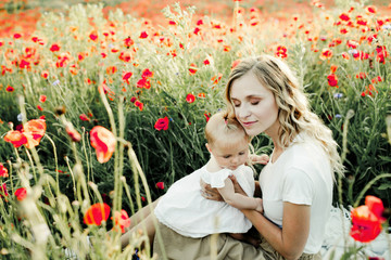woman snuggles to her baby on the poppy field
