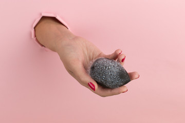 Girl hand holds a beauty blender for makeup from a hole in a pink background, copy space. Sponge in soapy foam, how to clean.