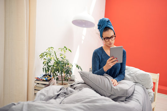 Gorgeous brunette with  towel on head using tablet while sitting on the bed in bedroom.