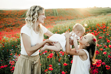 mother looks at her two daughters among the poppy field