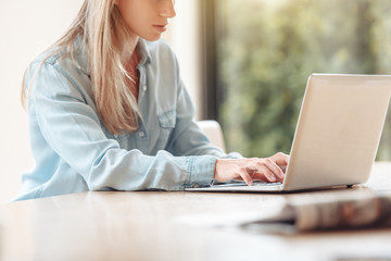 Side view of a young beautiful serious caucasian girl sitting at a table with a laptop and looking...