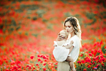 a woman hugs her baby among the poppy field