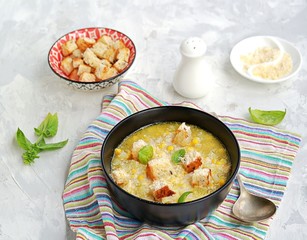 Summer soup of sweet corn and potatoes in a black bowl on a light gray concrete background. Served with croutons and grated parmesan cheese. Italian food. Selective focus.