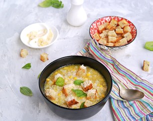 Summer soup of sweet corn and potatoes in a black bowl on a light gray concrete background. Served with croutons and grated parmesan cheese. Italian food. Selective focus.