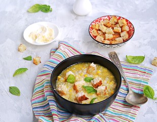Summer soup of sweet corn and potatoes in a black bowl on a light gray concrete background. Served with croutons and grated parmesan cheese. Italian food. Selective focus.