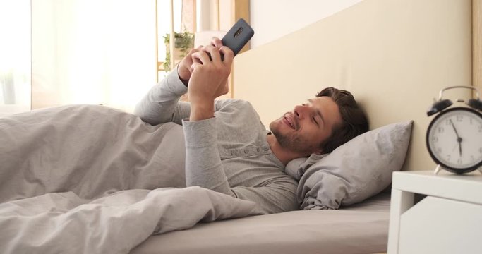 Happy man using mobile phone lying in bed