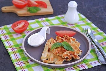 Savory zucchini waffles on a white plate on a dark concrete background. Served with ranch dressing and fresh tomato. Healthy food.